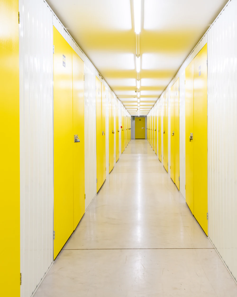 A bright hallway of yellow self-storage unit doors